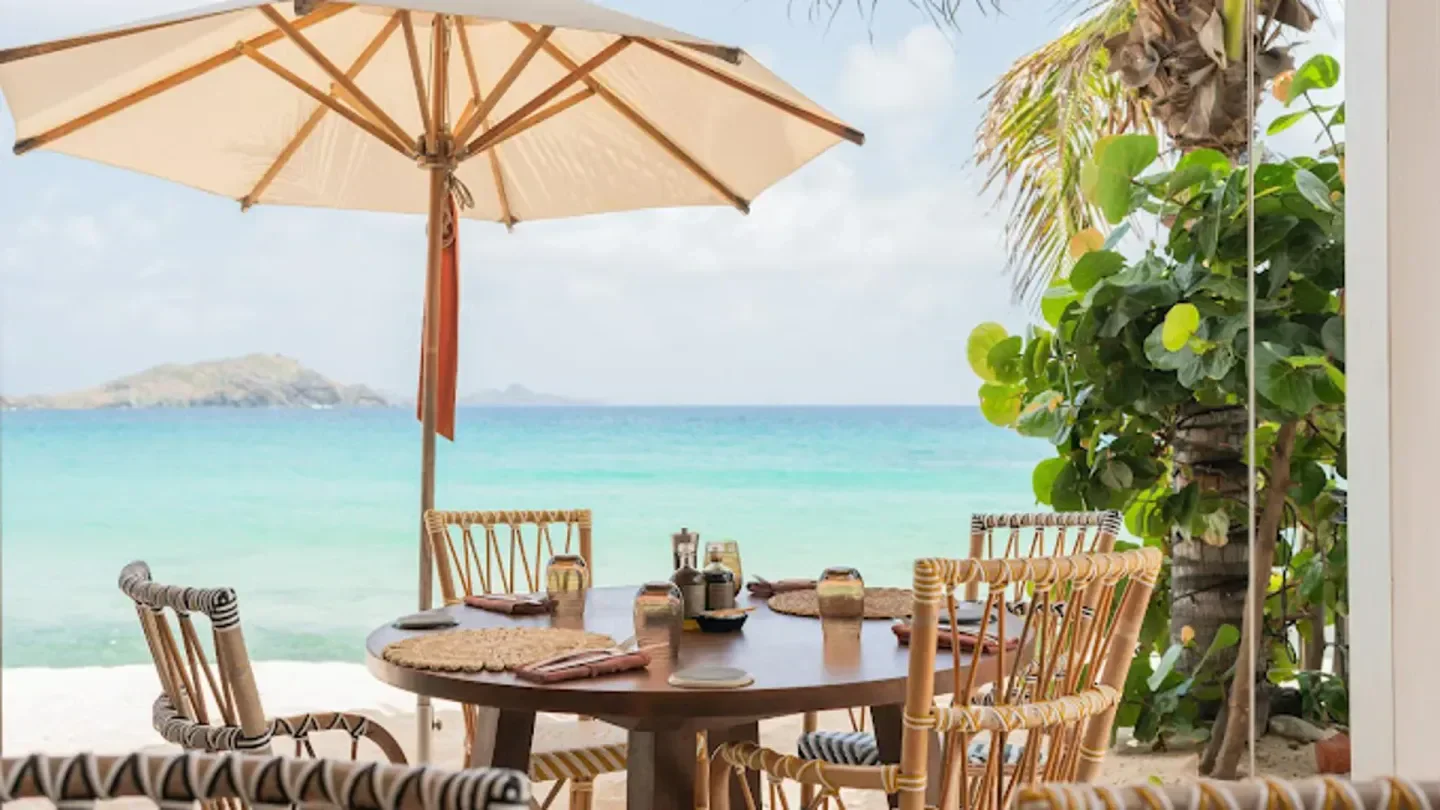 Beachfront dining at La Cabane in St. Barts with ocean views, table set and umbrella.